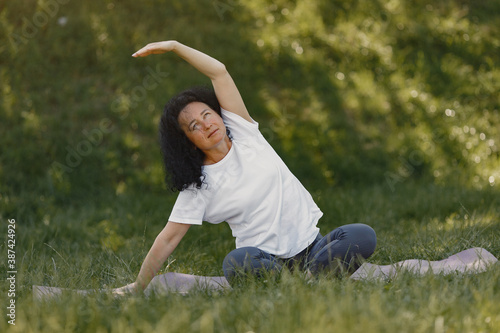 Mature lady training in a summer park. Brunette doing yoga. Old woman in a sports clothes.