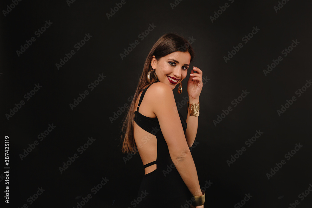 Portrait of laughing charming woman in evening dress with bare back and golden jewelry posing over black background Portrait of laughing charming woman in evening dress with bare back and golden jewelry posing over black background