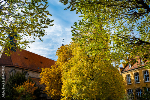 Old German stone church surrounded by autumn trees in orange & yellow. Taken in a park in Feuchtwangen in Fall.