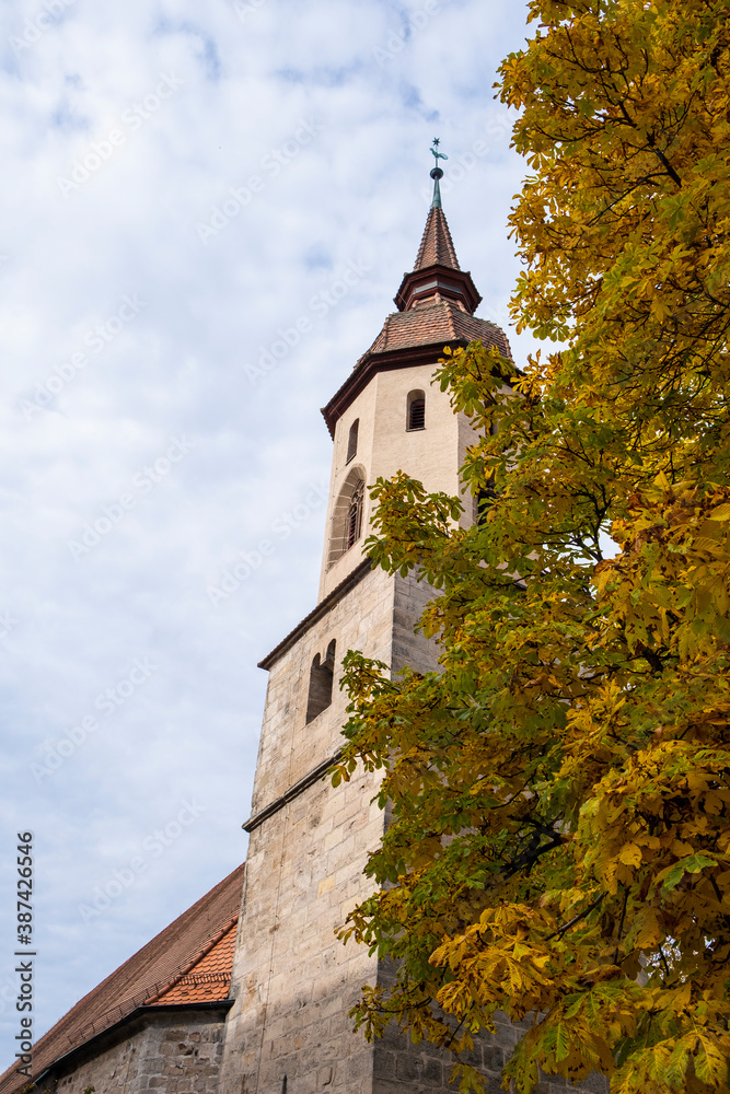 Old German stone church surrounded by autumn trees in orange & yellow. Taken in a park in Feuchtwangen in Fall.