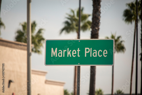 A green street sign that says Marketplace with palm trees and a blue sky background