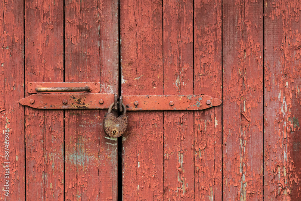 Locked old red double door with rusty padlock. Peeled door Locked old red double door with rusty padlock. Peeled door