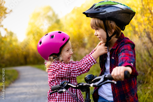 Slika na platnu A cute little girl helps her brother put on a Bicycle helmet