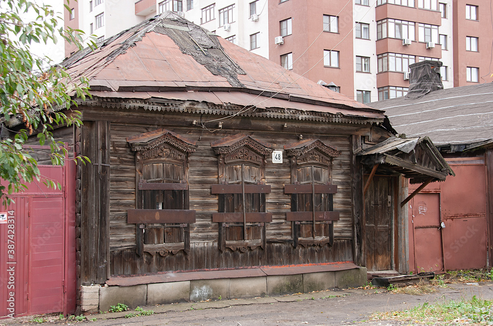 Old house with carved wooden facade details against the background of a new multi-storey building Old house with carved wooden facade details against the background of a new multi-storey building