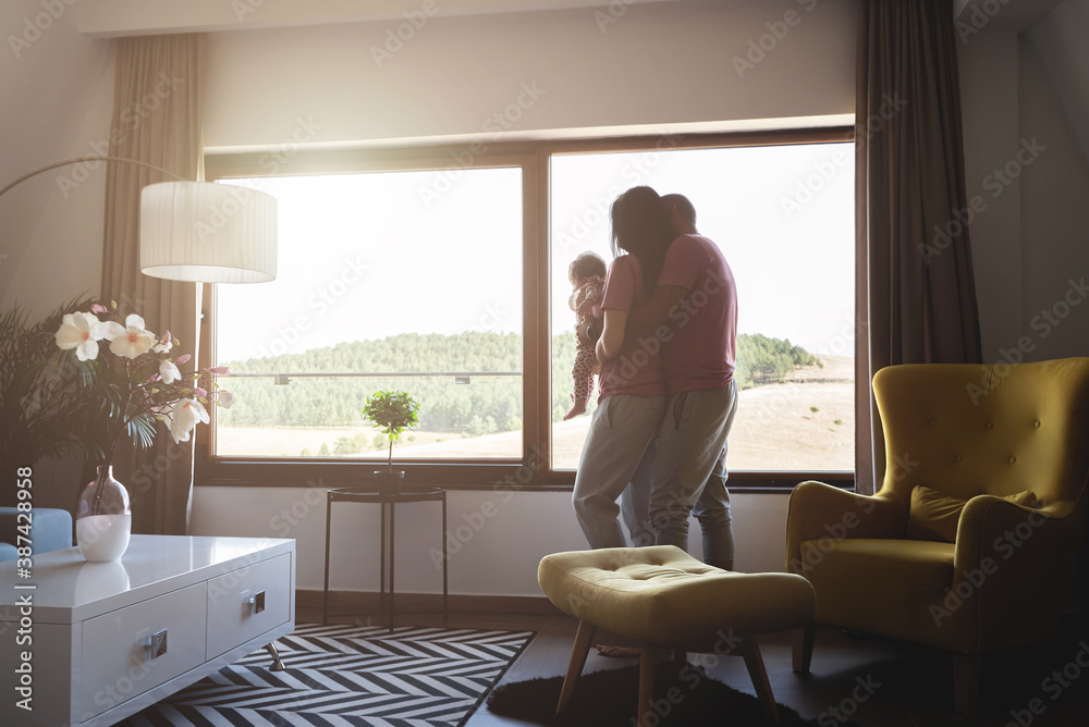 Loving parents with baby daughter near house window