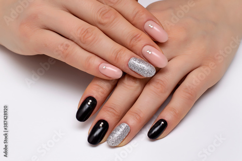 Black  beige  silver  shiny manicure with crystals on short oval nails close-up on a white background.