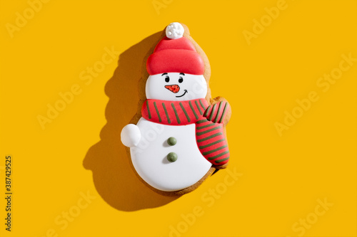 Snowman biscuit. Christmas bakery food. Winter holidays homemade dessert. Cute fun gingerbread cookie decorated with white red icing for kids isolated on orange background.