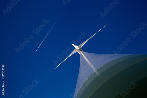 Huge wind turbine with blue sky and plane with contrail © Yann Wirthor