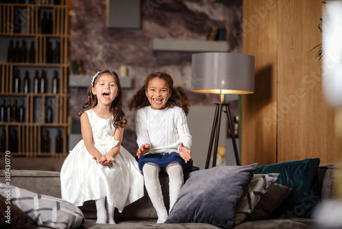 Two beautiful little girls are sitting on the back of sofa.