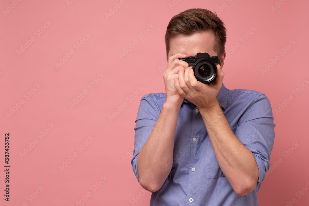Traveler and photographer. Studio portrait of handsome young man holding photocamera taking photo. Yellow blackground. - obrazy, fototapety, plakaty 