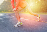 Runner stretching legs on asphalt road with vegetation in the background. Healthy life. Athlete.