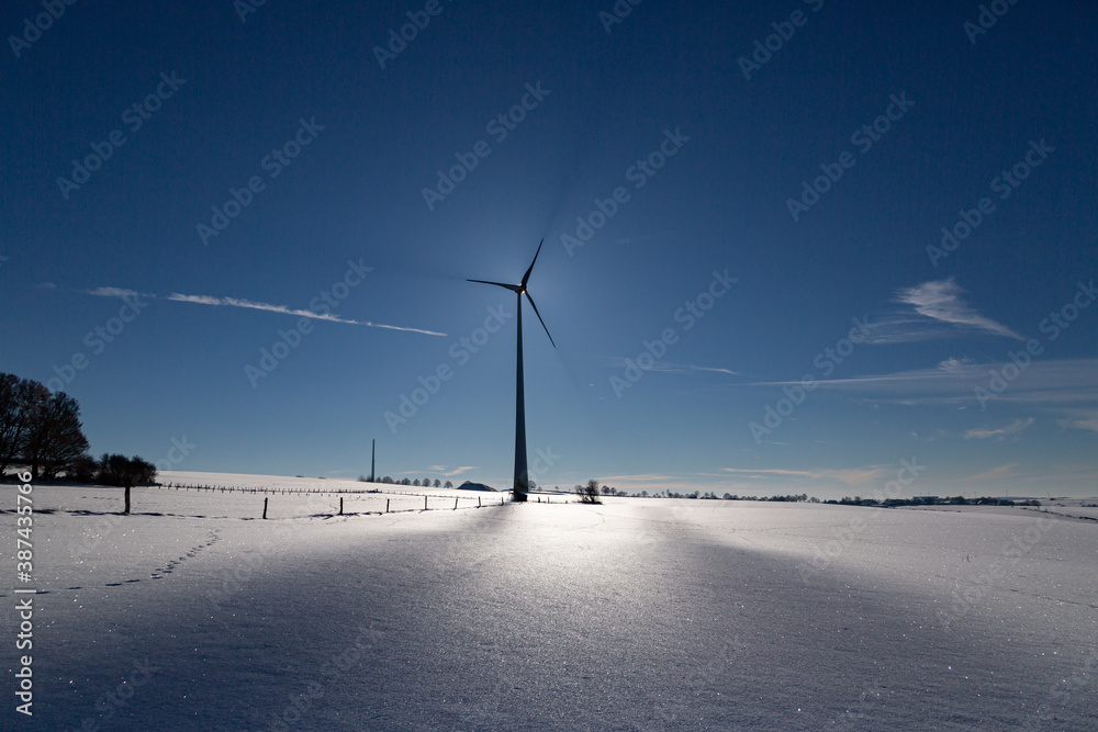 Wind Turbine in winter on a field with sunflare and shadows of the blades