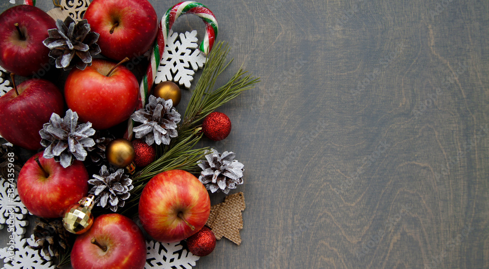Christmas background with pine branches, red apples and snowy cones. Dark wooden table.Top view. Space for text.