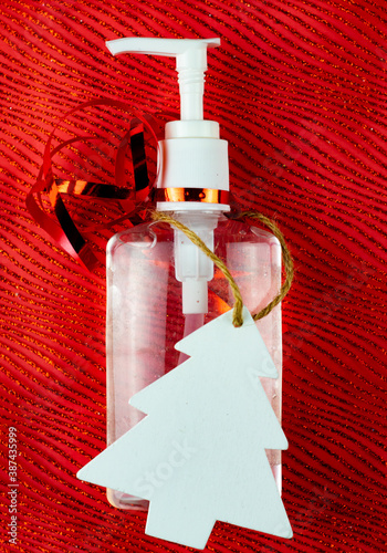 Bottle of hand gel sanitizer with Christmas decoration and ribbon as a gift. Concept of spending Christmas during coronavirus pandemic lock down and quarantine.