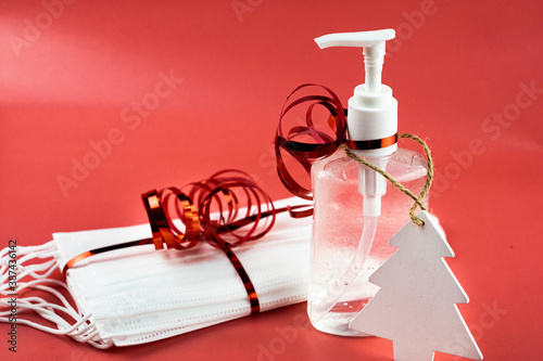Obraz na płótnie Bottle of hand gel sanitizer and protective masks with Christmas decoration and ribbon as a gift. Celebrating Christmas during coronavirus pandemic lock down and quarantine. Pink background. w salonie