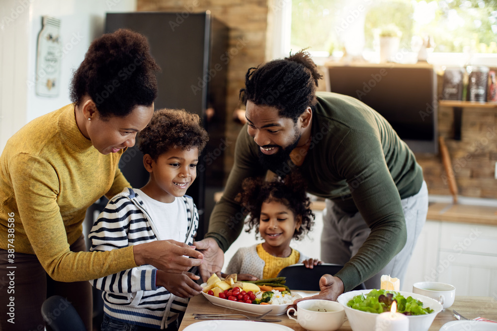 Happy African American family serving food at dining table. Happy African American family serving food at dining table.