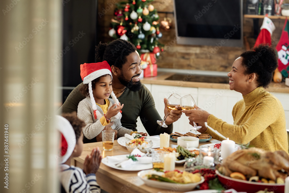Happy black parents toasting with wine during family lunch on Christmas day.