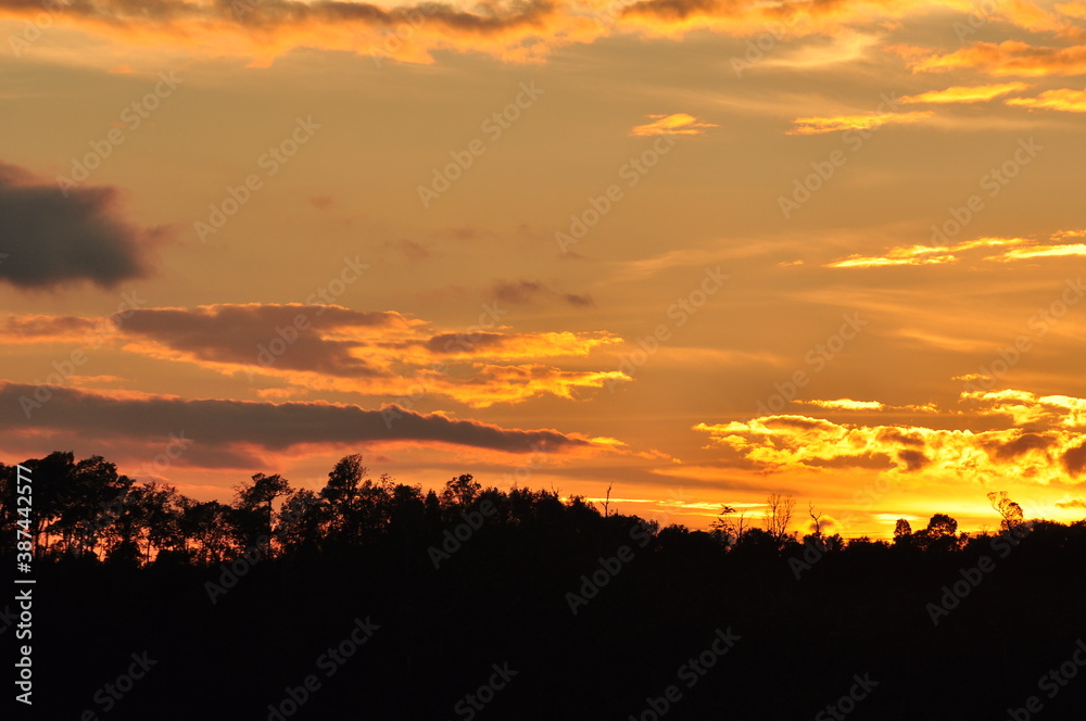 Picture of a sun setting behind a dense forest area followed by mountains. Picture of a sun setting behind a dense forest area followed by mountains.