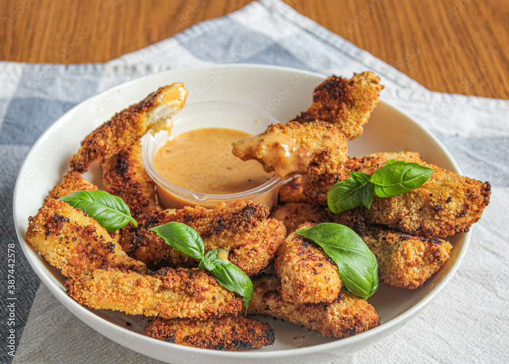 Chicken finger being dipped into the sauce. breaded and baked chicken finger eaten as an appetiser. Female hand holding chicken finger. 