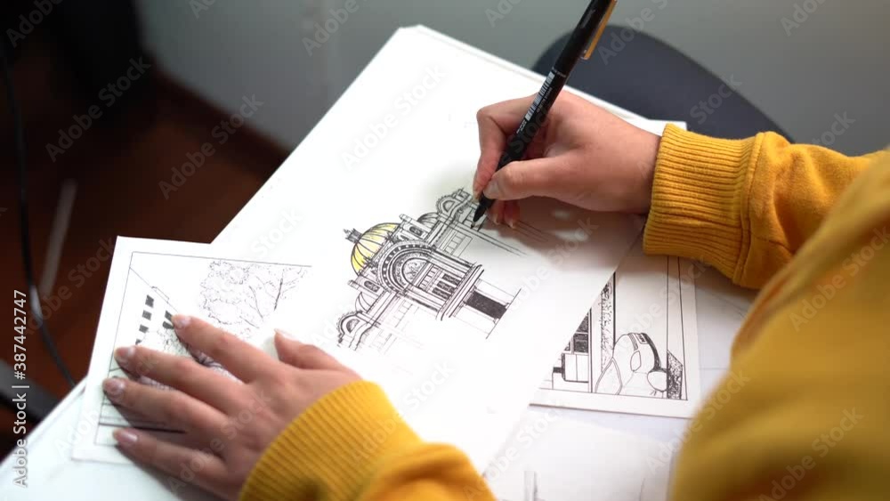 Hands of a girl drawing a building in a paper wearing a yellow hoddie