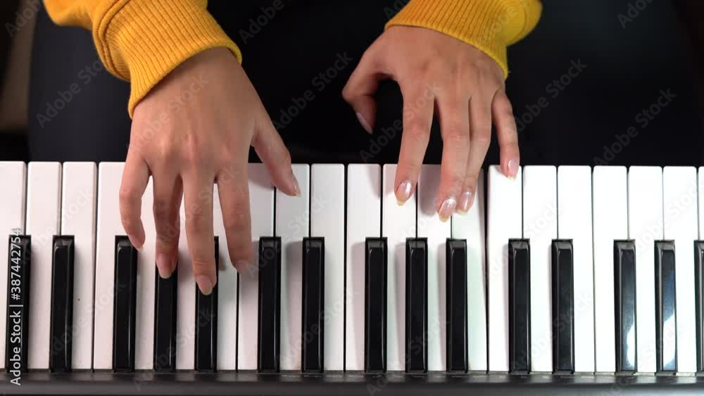 Cenital frame of a girl hands playing piano with a yellow hoddie
