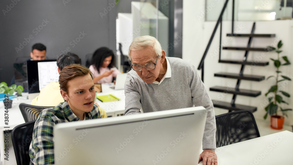 Aged man, senior worker training, mentoring, giving advice to new employee while standing in the office
