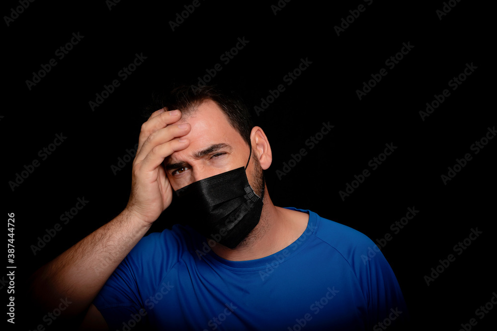 Bearded man dressed in blue t-shirt and with a black mask to protect himself from coronavirus posing against black background Bearded man dressed in blue t-shirt and with a black mask to protect himself from coronavirus posing against black background