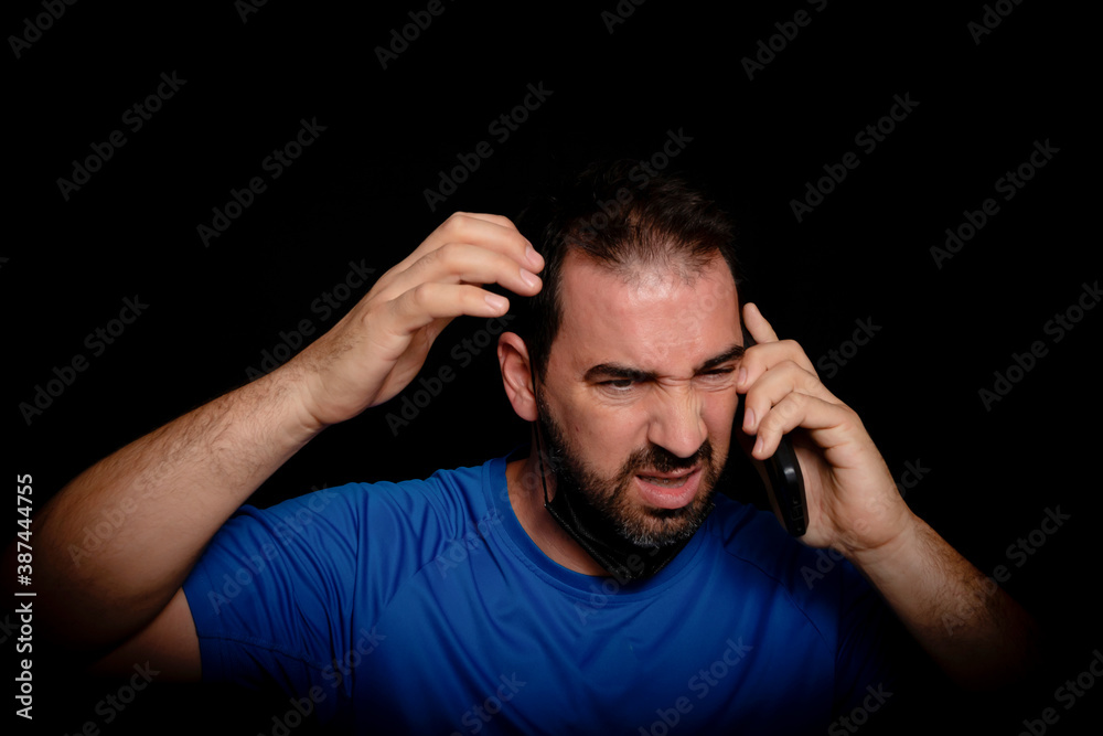 Bearded man dressed in blue t-shirt and with a black mask to protect himself from coronavirus posing against black background Bearded man dressed in blue t-shirt and with a black mask to protect himself from coronavirus posing against black background
