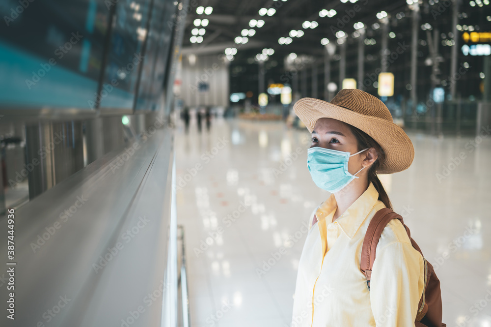 Asian woman wearing protective mask looking at time table screen departure schedule in an airport terminal. Concept of safety travel, coronavirus pandemic and new normal Asian woman wearing protective mask looking at time table screen departure schedule in an airport terminal. Concept of safety travel, coronavirus pandemic and new normal
