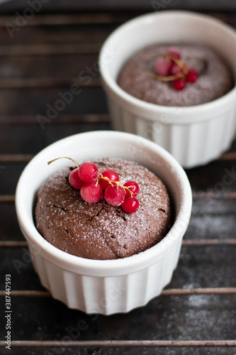 Chocolate fondant in the white ramekin with red currant on the dark background