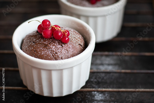 Chocolate fondant in the white ramekin with red currant on the dark background
