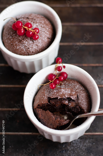 Chocolate fondant in the white ramekin with red currant on the dark background