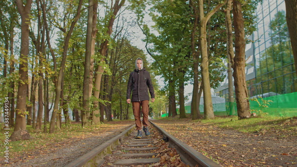 A young guy confidently moves to the camera in the park on the track, a stylishly dressed teenager.