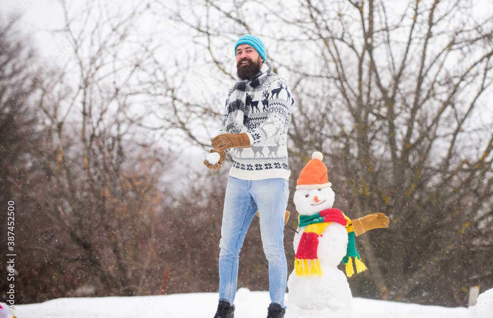 Man cheerful bearded hipster knitted hat and warm gloves play with snowman snow outdoors. Have fun winter day. Let it snow. Christmas holidays. Active lifestyle. Snow games. Leisure on fresh air