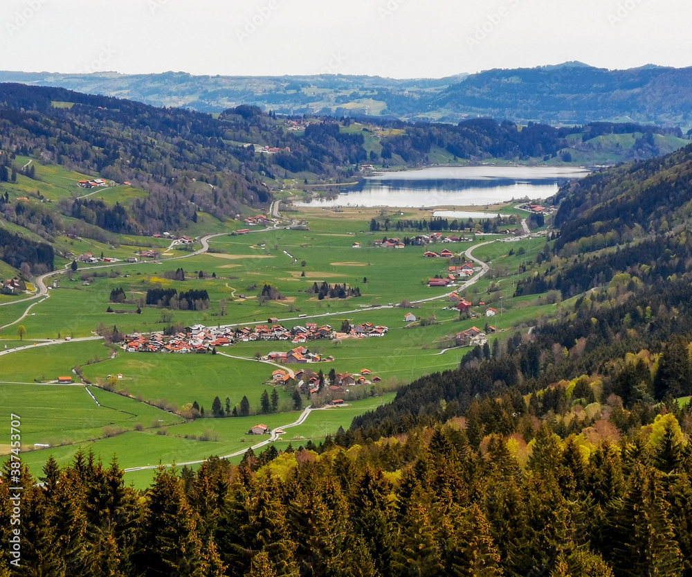 Aeria view of lake Großer Alpsee with small village and valley in front a mountains in the background