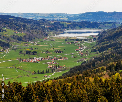 Aeria view of lake Großer Alpsee with small village and valley in front a mountains in the background