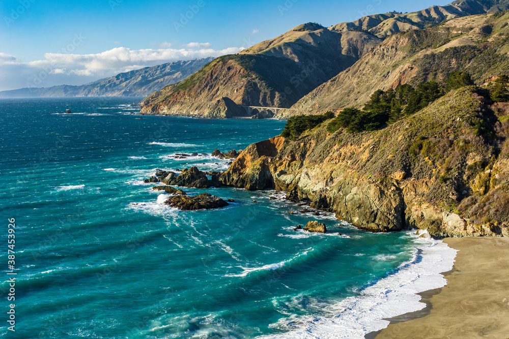 Turquoise ocean water fills a beautiful, rocky cove in Big Sur with the Big Creek Bridge in the background
