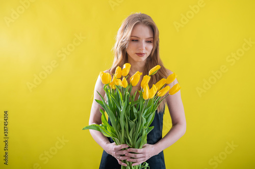Caucasian woman with an armful of yellow tulips on a yellow background. International Women's Day. Bouquet of spring flowers
