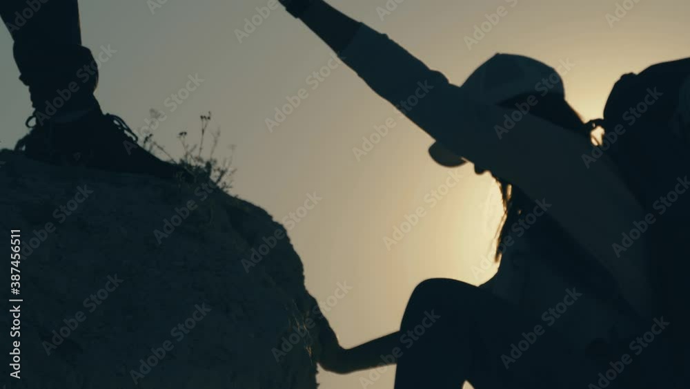 Silhouette of helping hand between two climber. two hikers on top of the mountain, a man helps a man to climb a sheer stone. couple hiking help each other silhouette in mountains with sunlight.
