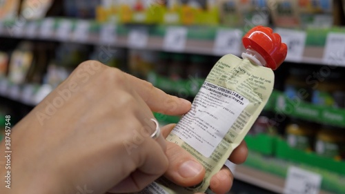Close up of female hand holding baby product to read label information in store. Shopping concept