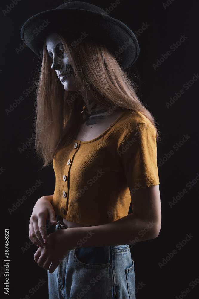 Girl with a skeleton make-up on her face on a dark background with a sad expression