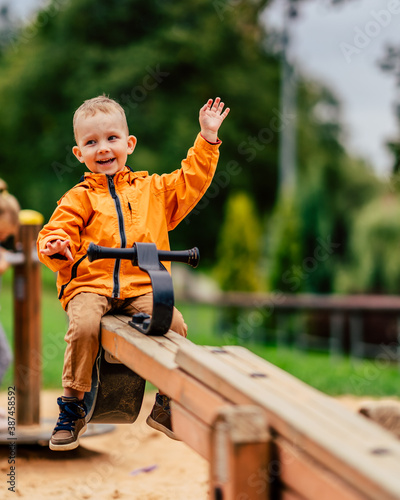 Happy kid waving from swings in playground - green background
