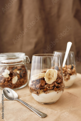 Close up of delicious layered dessert in glass jar, Homemade yogurt with granola and banana, Granola baked with nuts and honey
