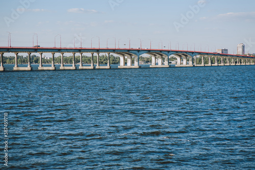 A large high concrete bridge stands in the water, sea, river against the background of the city.