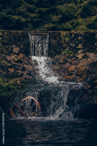 Water flows over the dam and creates a beautiful waterfall lit by the morning sun. Cascades in the Jizera Mountains, Czech Republic. A magical place in the forgotten wilderness photo