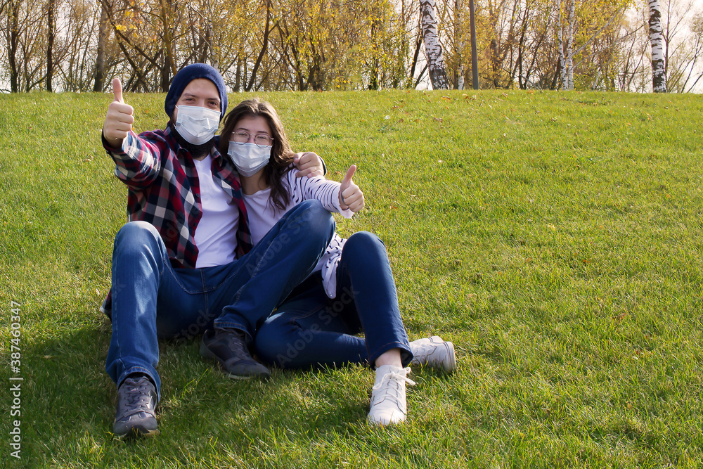 a guy and a girl are sitting on the lawn in protective medical masks