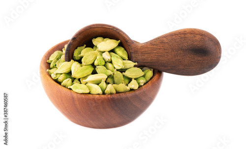 Cardamom seeds in wooden bowl and spoon, isolated on white background. Pile of green cardamom.