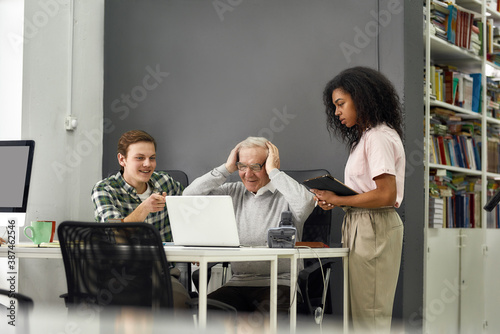 Too much information, Aged man senior intern touching head with hands while listening to his young colleagues, Friendly workers training, teaching new employee