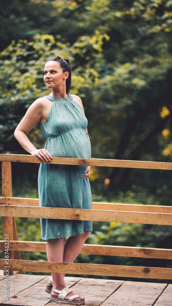 Naklejka premium Pregnant woman in a dress walking through the forest. Portrait of a young, pregnant woman. 