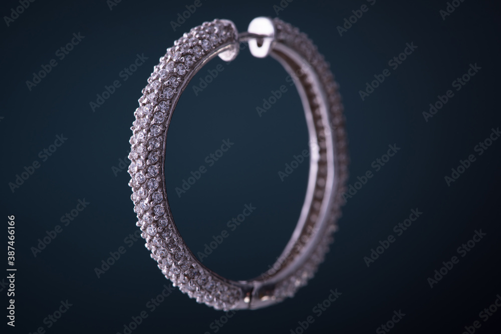 White gold diamond earring with zircon on the blue background. Circle shape